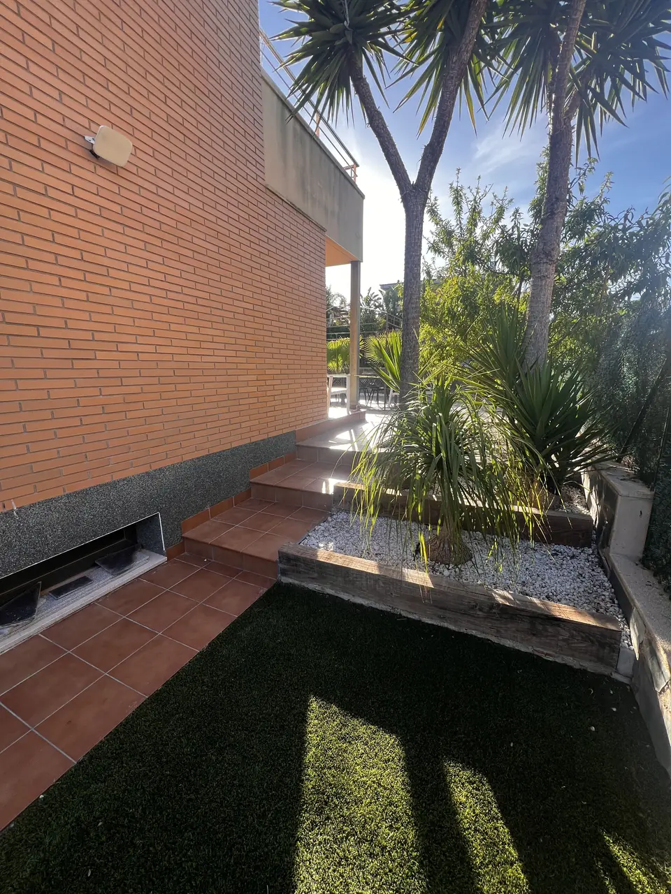 Césped artificial con yucas y parterre de canto blanco junto a una escalera de terracota