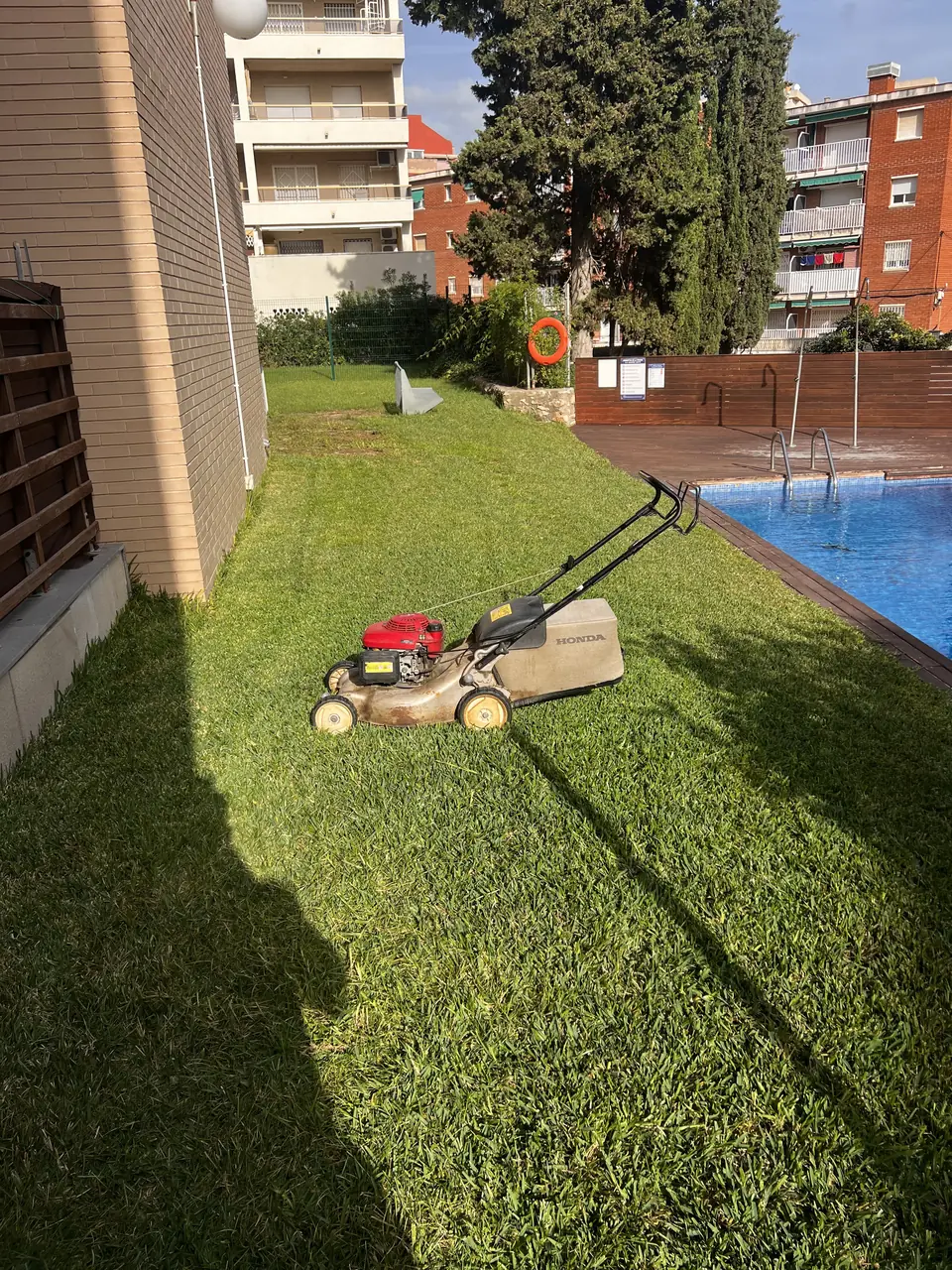 Corte del césped junto a la piscina de una comunidad de vecinos