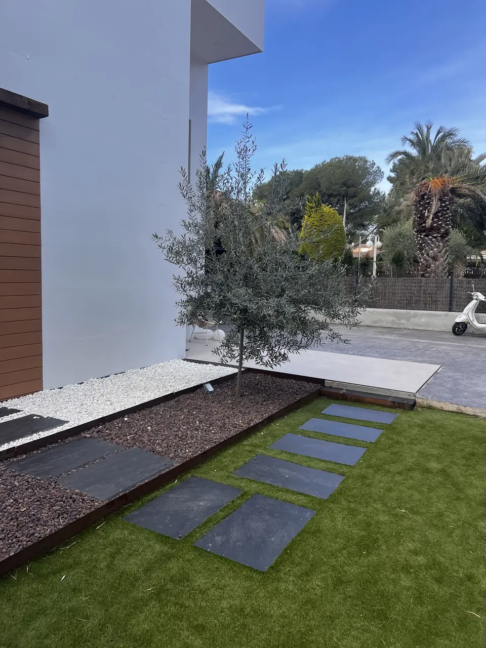 Jardín diseñado por nosotros con olivo, grava, canto blanco y losas de paso sobre césped artificial