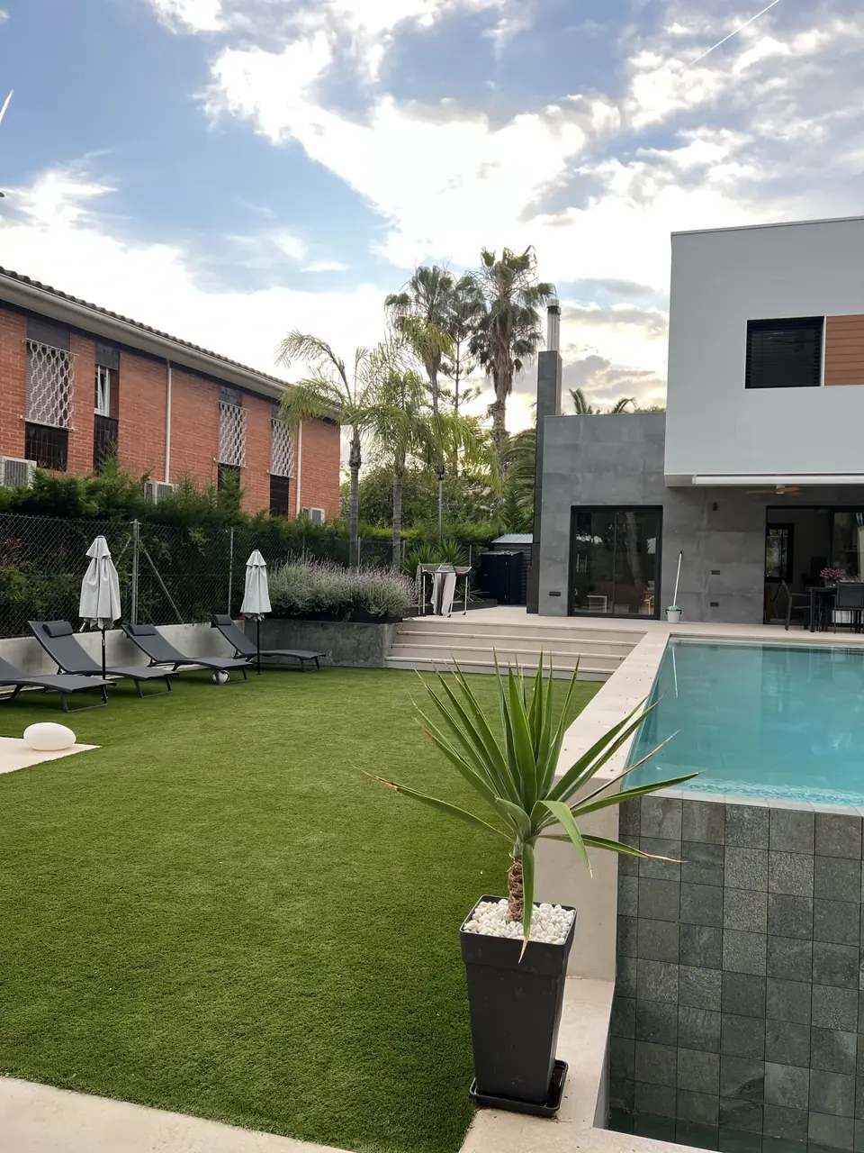 Jardín de una villa con piscina, césped artificial y palmeras que mantenemos en el Tarragonès